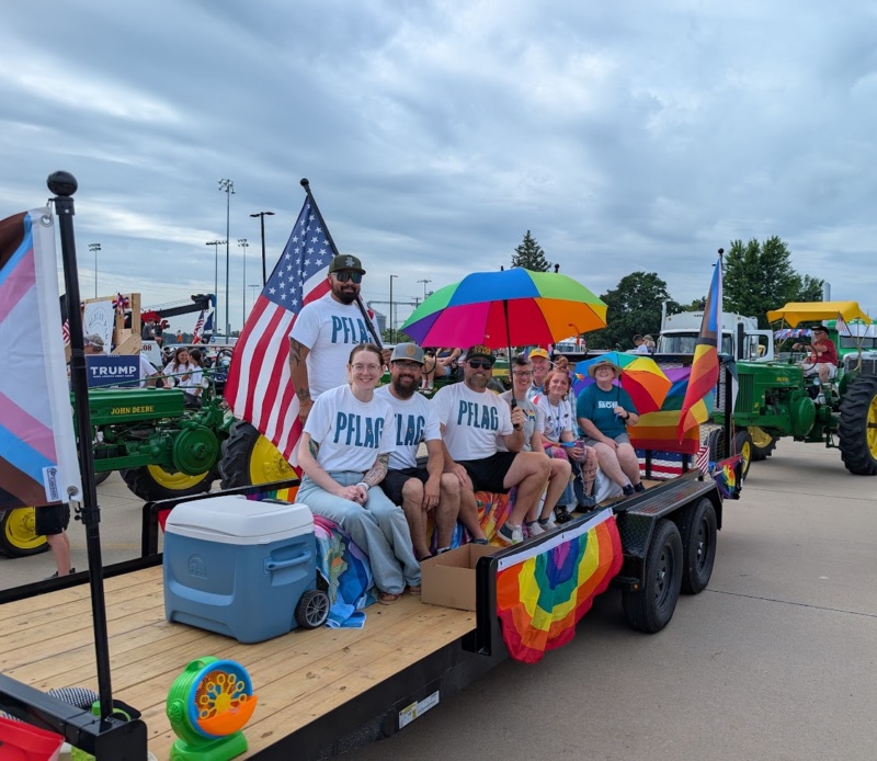 Several people on a trailer decorated with rainbows and US flags.